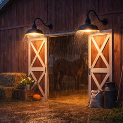 Two waterproof black gooseneck barn lights lighting up a rustic red barn door in the rain.